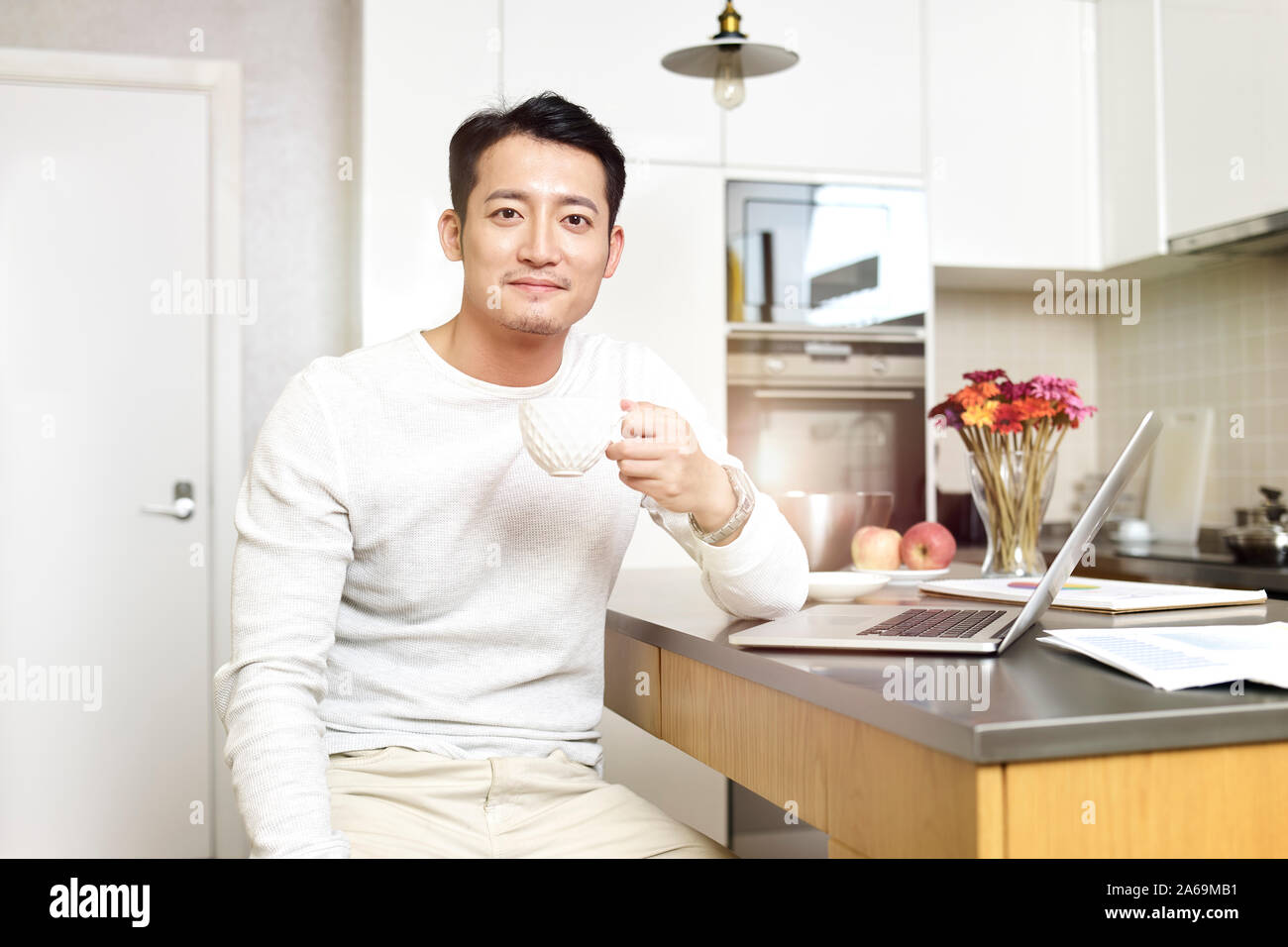portrait of a young asian man working from home holding a cup of coffee looking at camera smiling Stock Photo