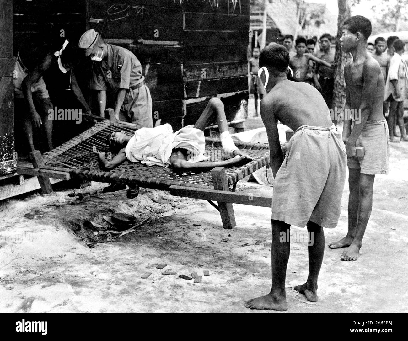An emaciated coolie too weak to walk is carried on a charpoy by fellow-coolies at the Japanese labor camp at Seletah, in the northern part of Singapore. Populated by about 1700 persons, including Javanese, the camp was discovered by the British accidentally. With their arrival an effort was made to clean up the camp and administer to the sick. Stock Photo