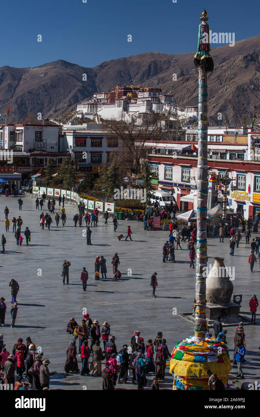 Tibetan pilgrims circumambulate around the Jokhang Temple in Barkhor Square in Lhasa, Tibet. In the background is the Potala Palace. Stock Photo