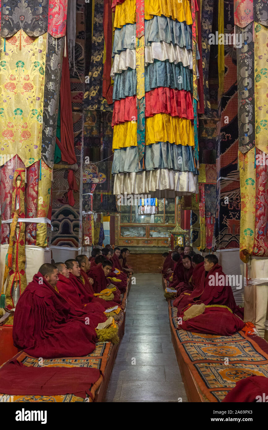 Buddhist monks worshipping under a fabric victory banner in Coqen Hall in the Ganden Buddhist