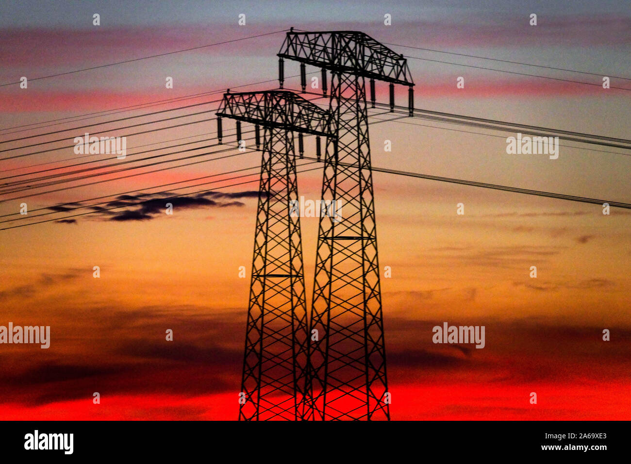 High voltage power lines sunset pylons transmission energy Germany Global warming climate change Sky wires connected to a plant Stock Photo