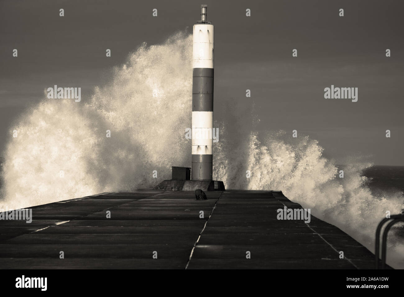 Wave breaking on jetty and beacon during storm at Aberystwyth in Wales. With colour toning Stock Photo