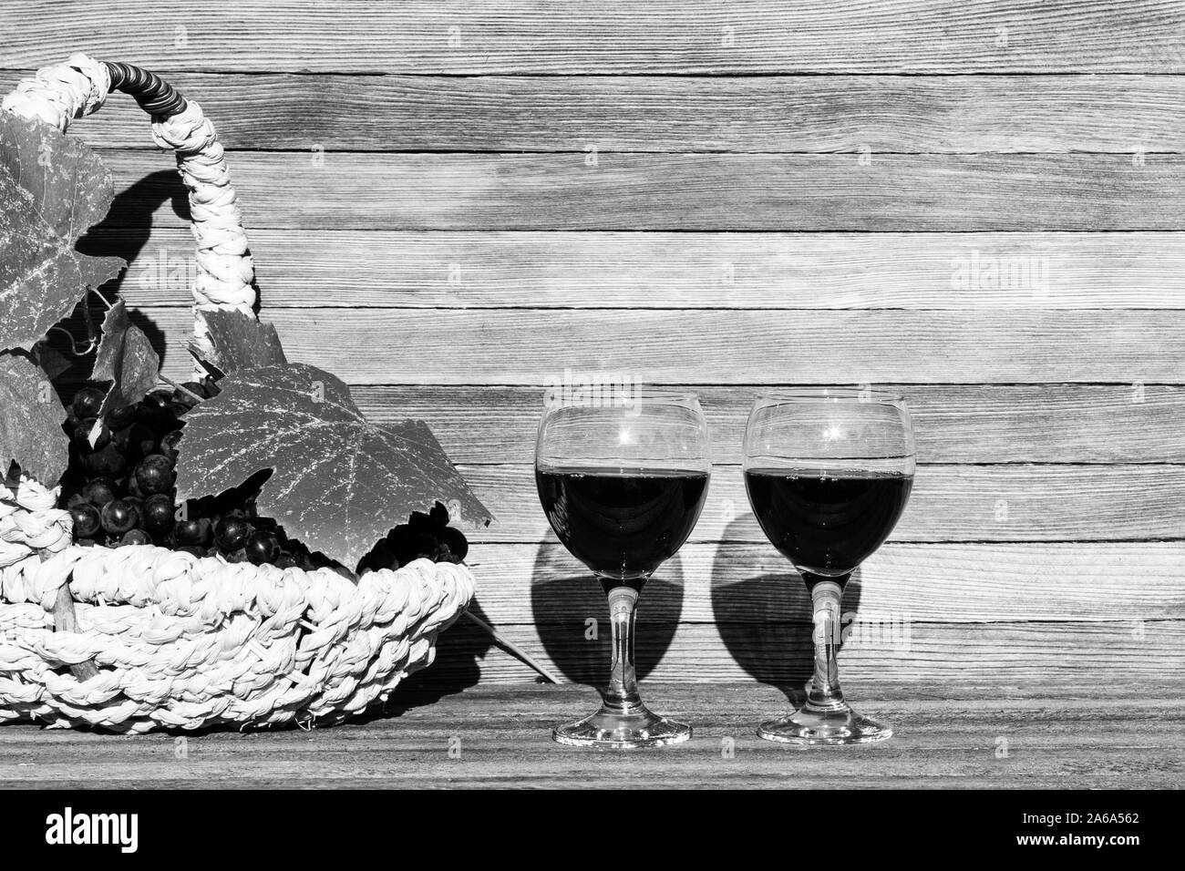 two glasses of red wine and a basket of grapes on a wooden background on a Sunny day with a copy of the space, black and white photo Stock Photo