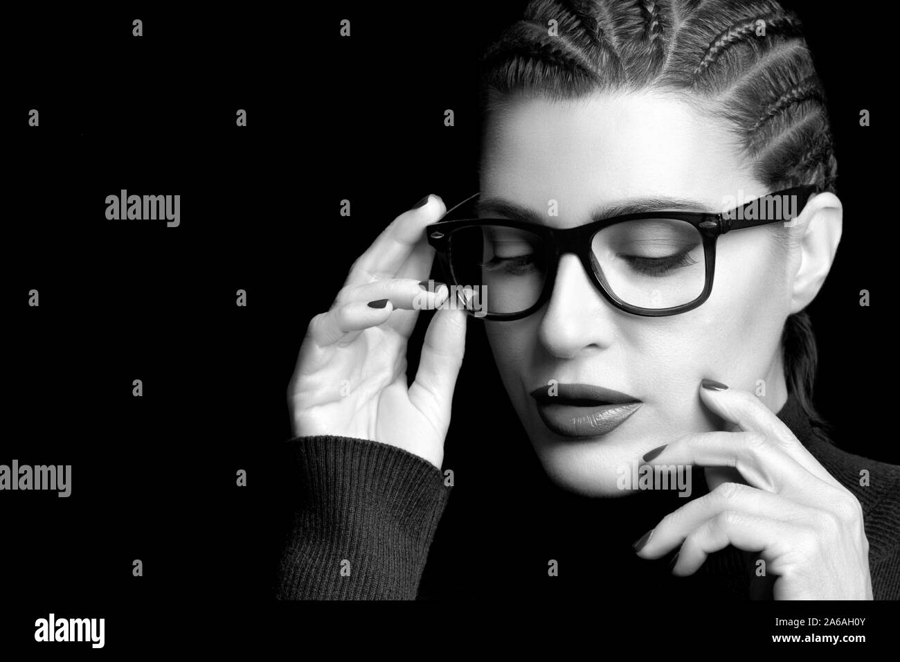 Monochrome beautiful elegant young woman with braided hair wear glasses or spectacles looking down with hand to the frame, Vision correction, optometr Stock Photo