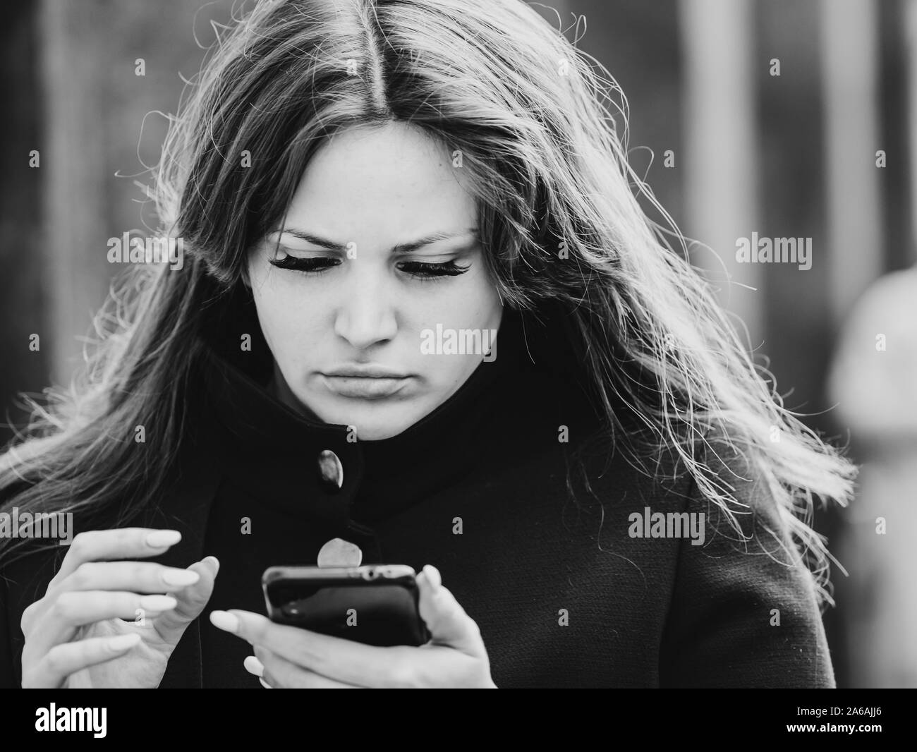 Moscow, Russia - October 19, 2019: A young woman is carefully looking at the smartphone screen that is in her hands. False eyelashes on the eyes. Blac Stock Photo