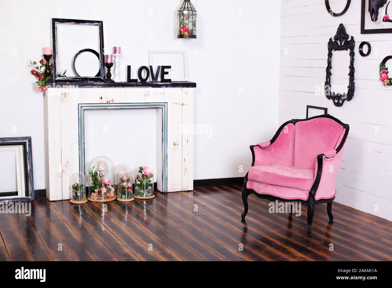 Vintage velor armchair, in a bright room and an artificial fireplace. Interior attic with wooden white walls. Picture frames on the wall. Stock Photo