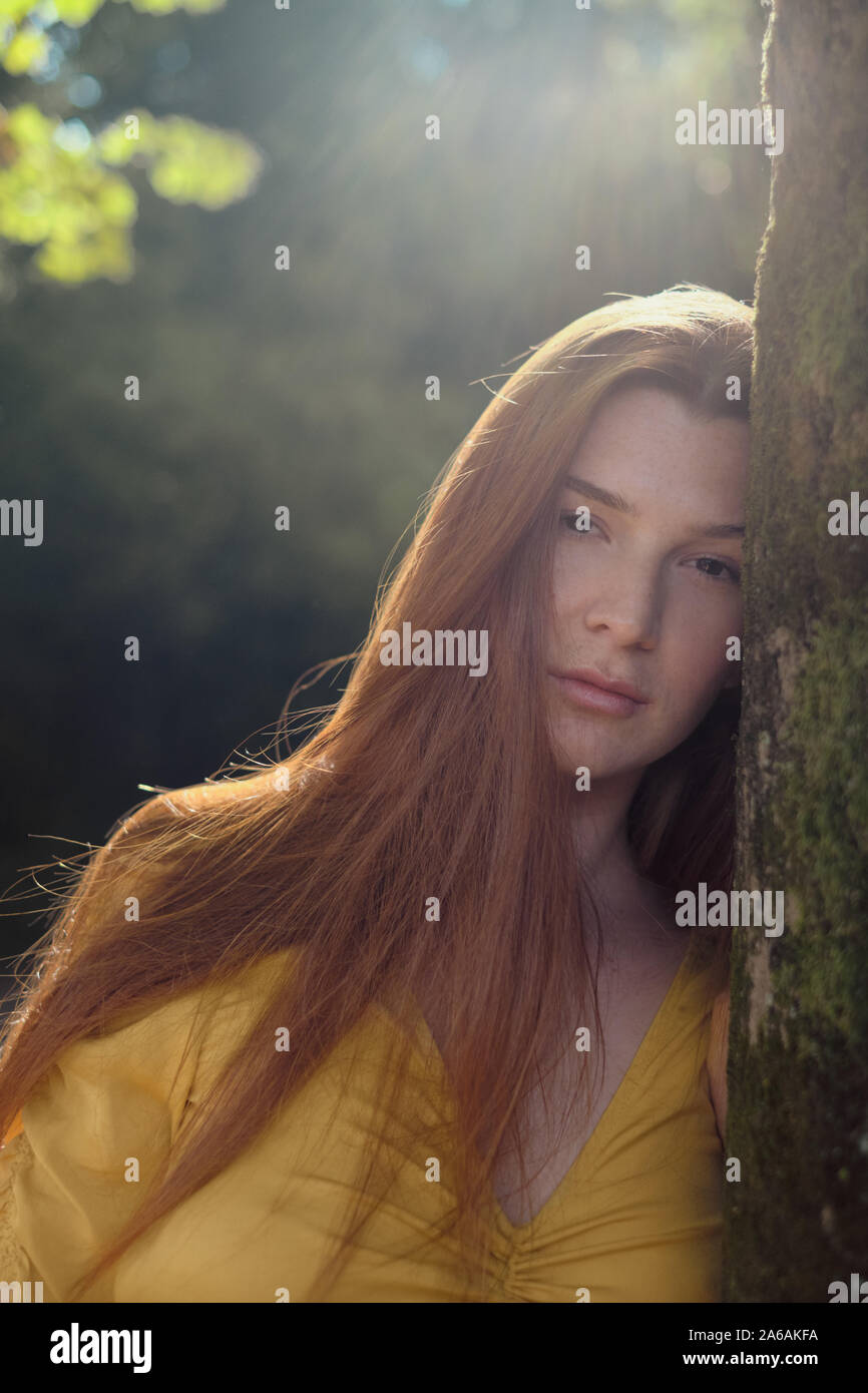 Portrait Of Redhead Young Woman Leaning On Tree Stock Photo