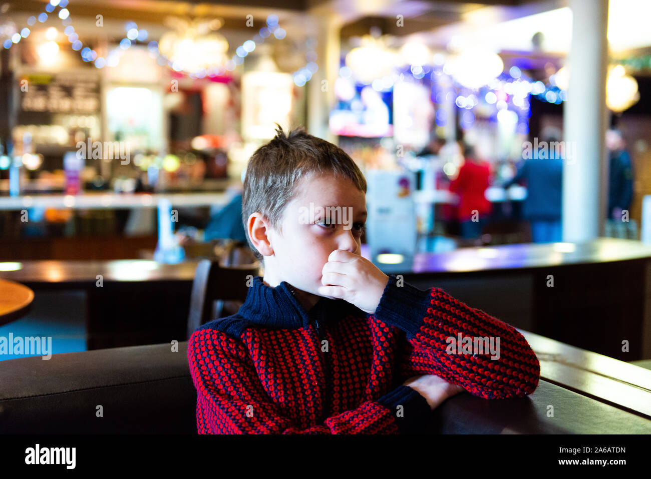 A handsome little boy with adhd, autism, apserger syndrome sits in a restaurant, pub waiting watching television at Yates in Newcastle Under Lyme Stock Photo