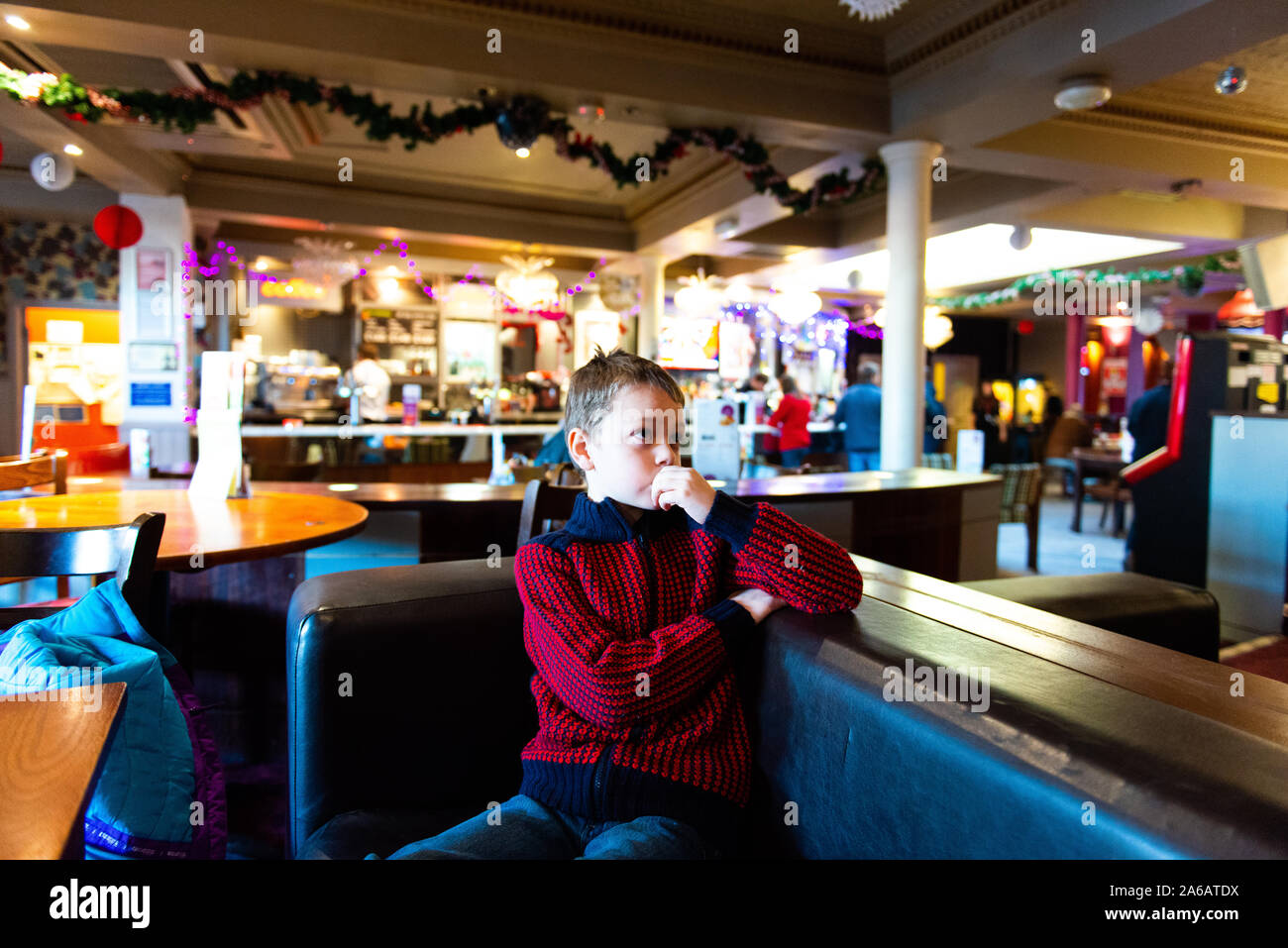 A handsome little boy with adhd, autism, apserger syndrome sits in a restaurant, pub waiting watching television at Yates in Newcastle Under Lyme Stock Photo