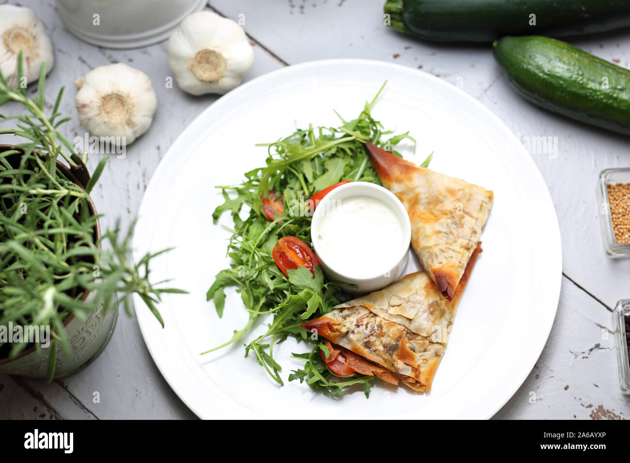 Vegetarian food. Dumplings made of filo dough stuffed with vegetables and mushrooms, served with garlic sauce and green salad Stock Photo