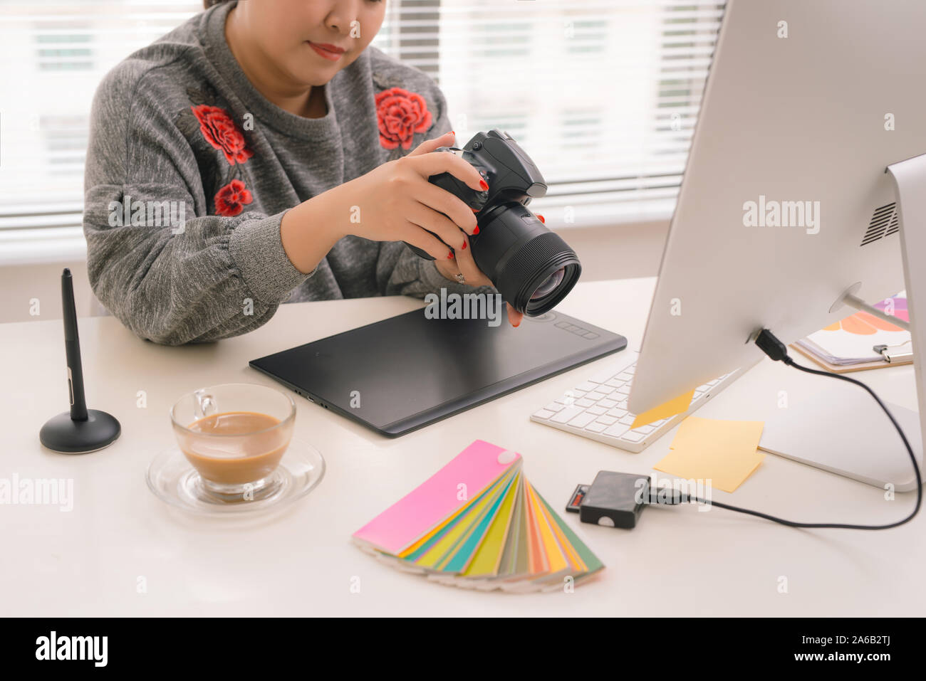 female freelancer photographer cheking photos on a digital camera while sitting at the table in workstation Stock Photo