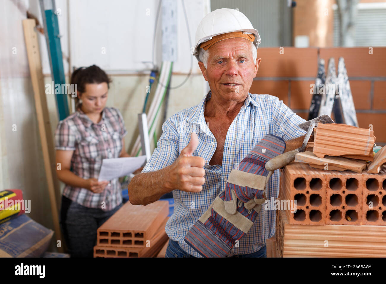 Happy experienced elderly bricklayer posing near red brick stack in building under construction Stock Photo