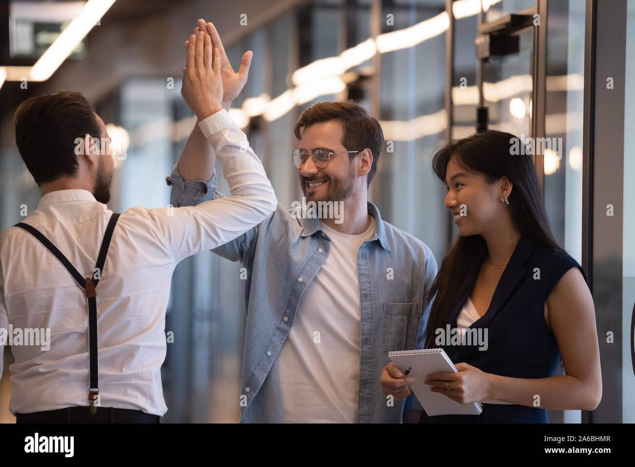 Happy employees colleagues giving high five, greeting in office hallway ...