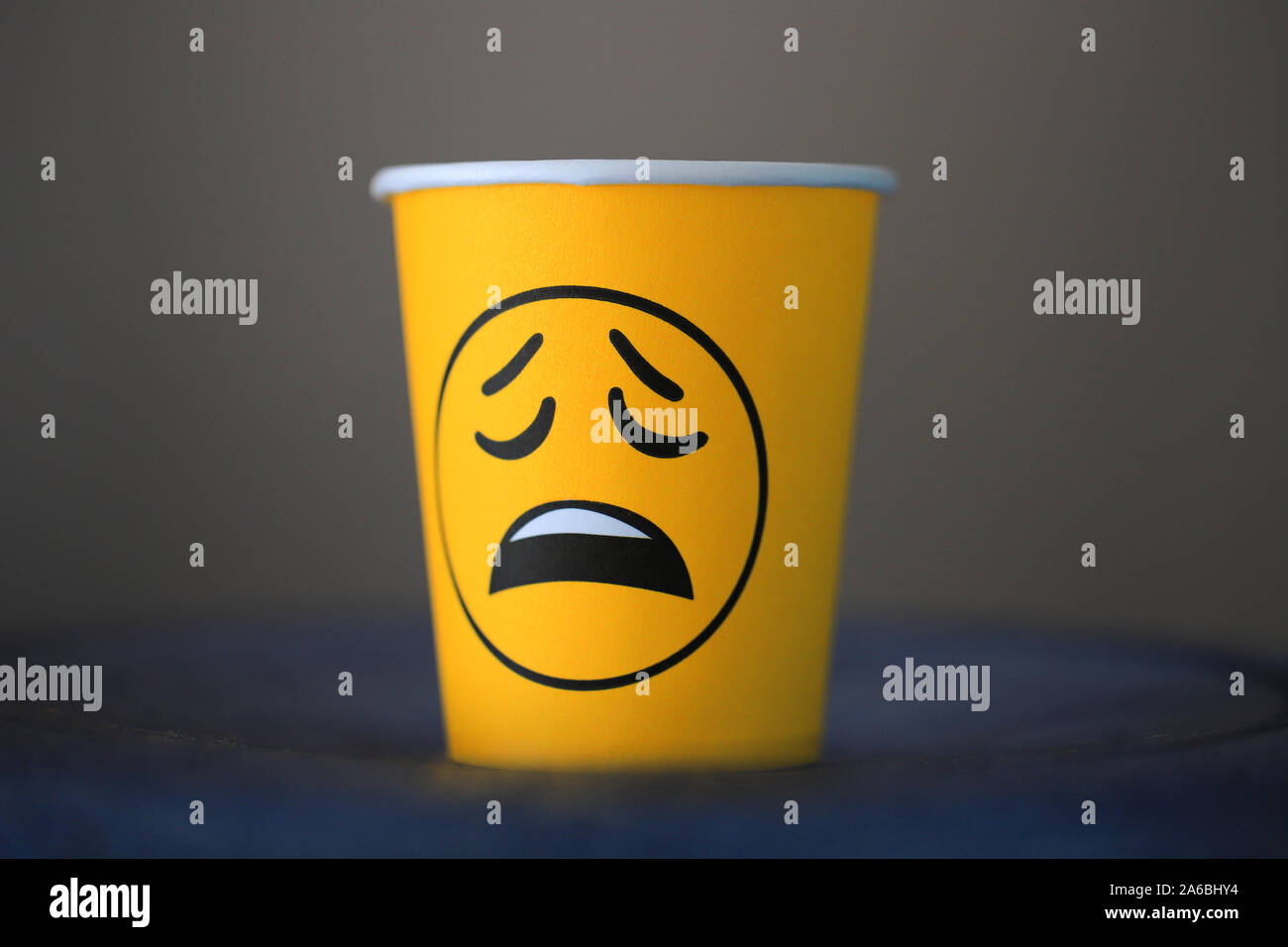 Sad emotion emoji on a paper cup with coffee in the office. Boring