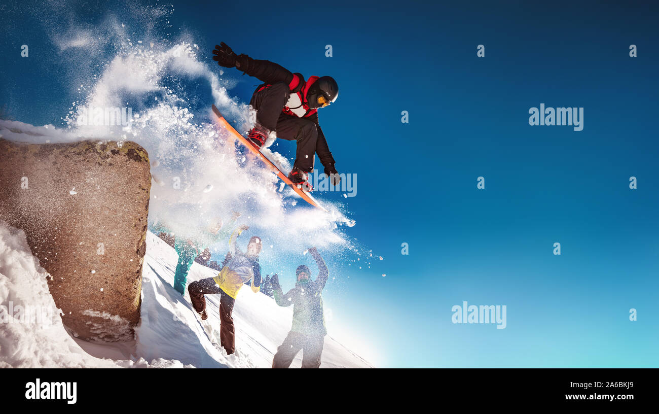 Snowboarder jumps from big rock against group of cheerleaders Stock Photo