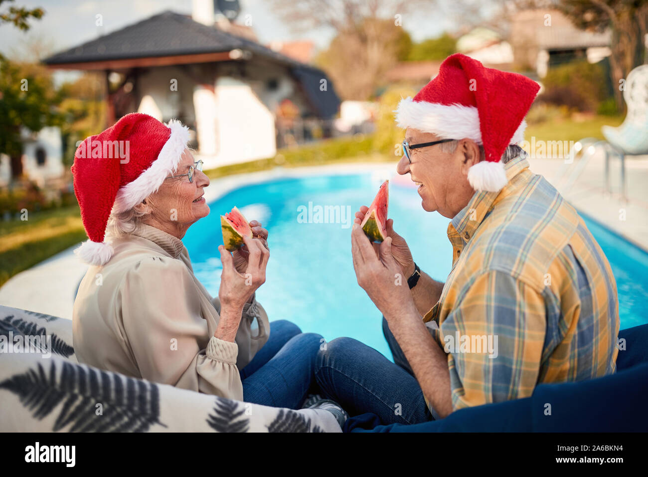 Smiling senior man and woman on christmas in Santa hats eating ...
