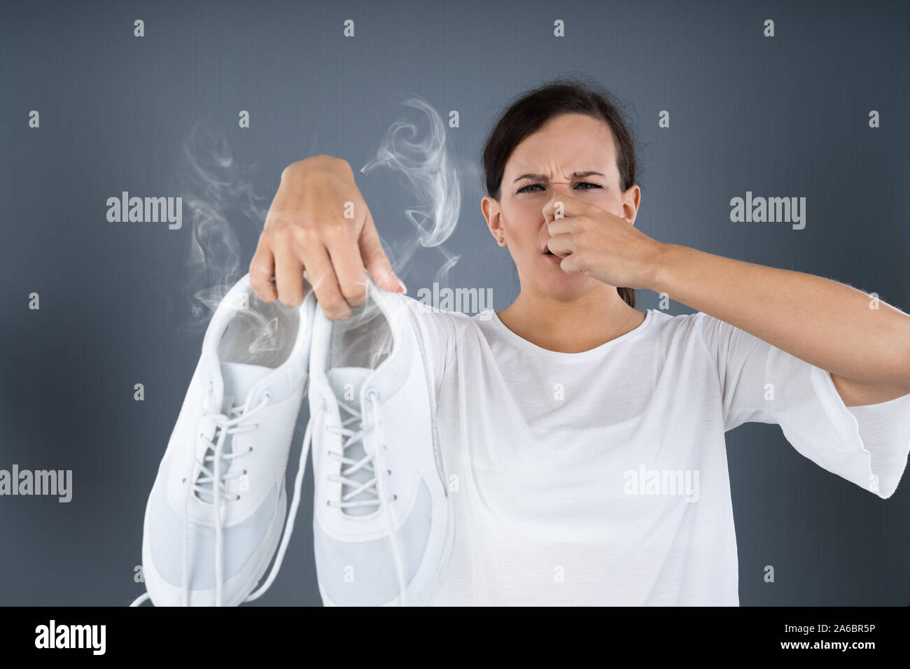 Close-up Of A Woman Covering Her Nose While Holding Stinky Shoes On Grey Background Stock Photo