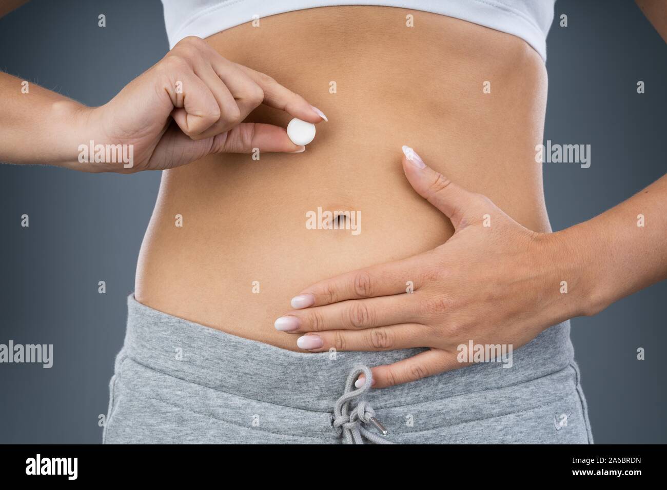 Woman Holding Pill In Front Of Her Stomach Stock Photo