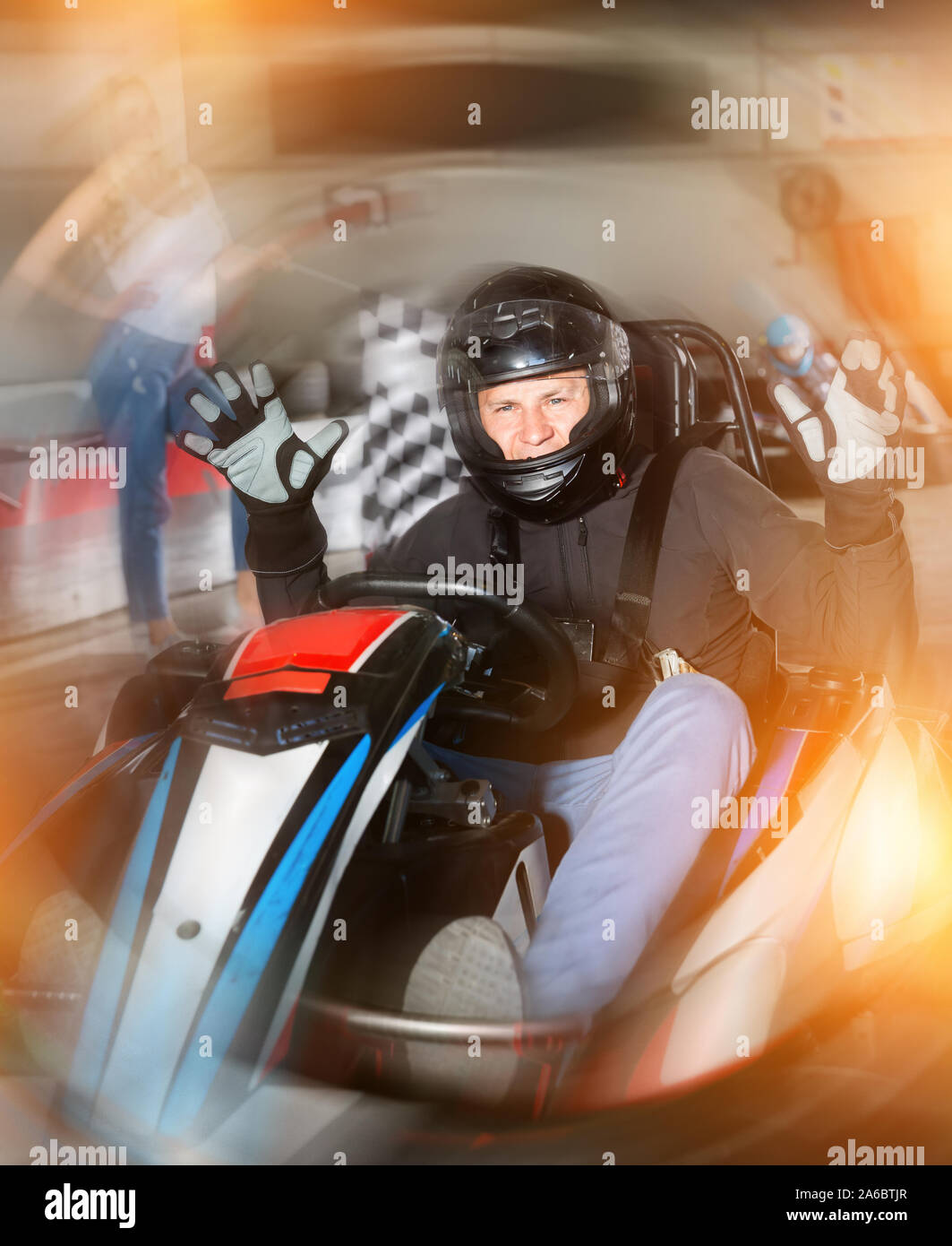 Portrait of male racer in helmet crossing a finish line on kart track ...
