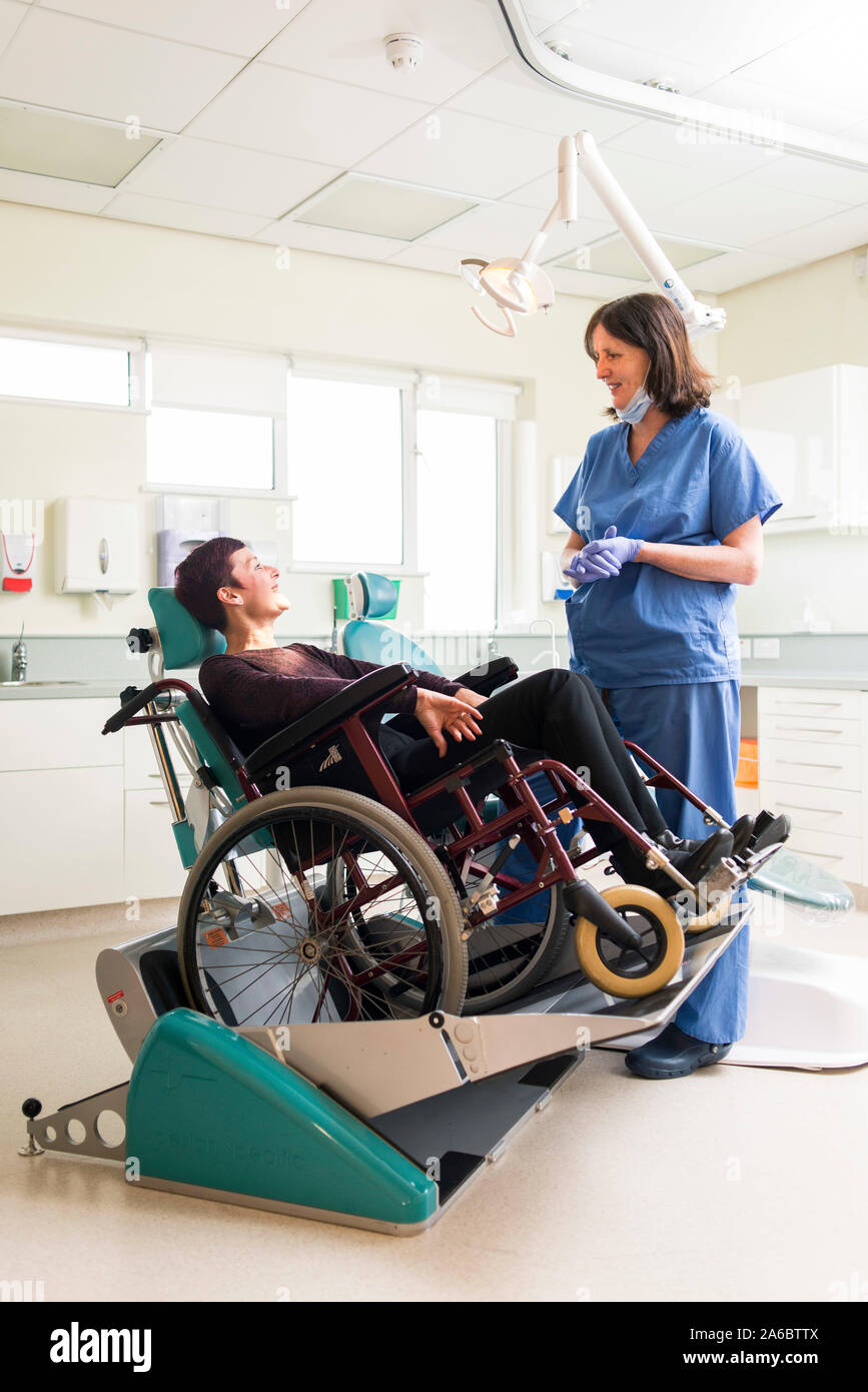 A dental nurse speaks to a disabled patient in a specialist wheelchair friendly dental chair Stock Photo