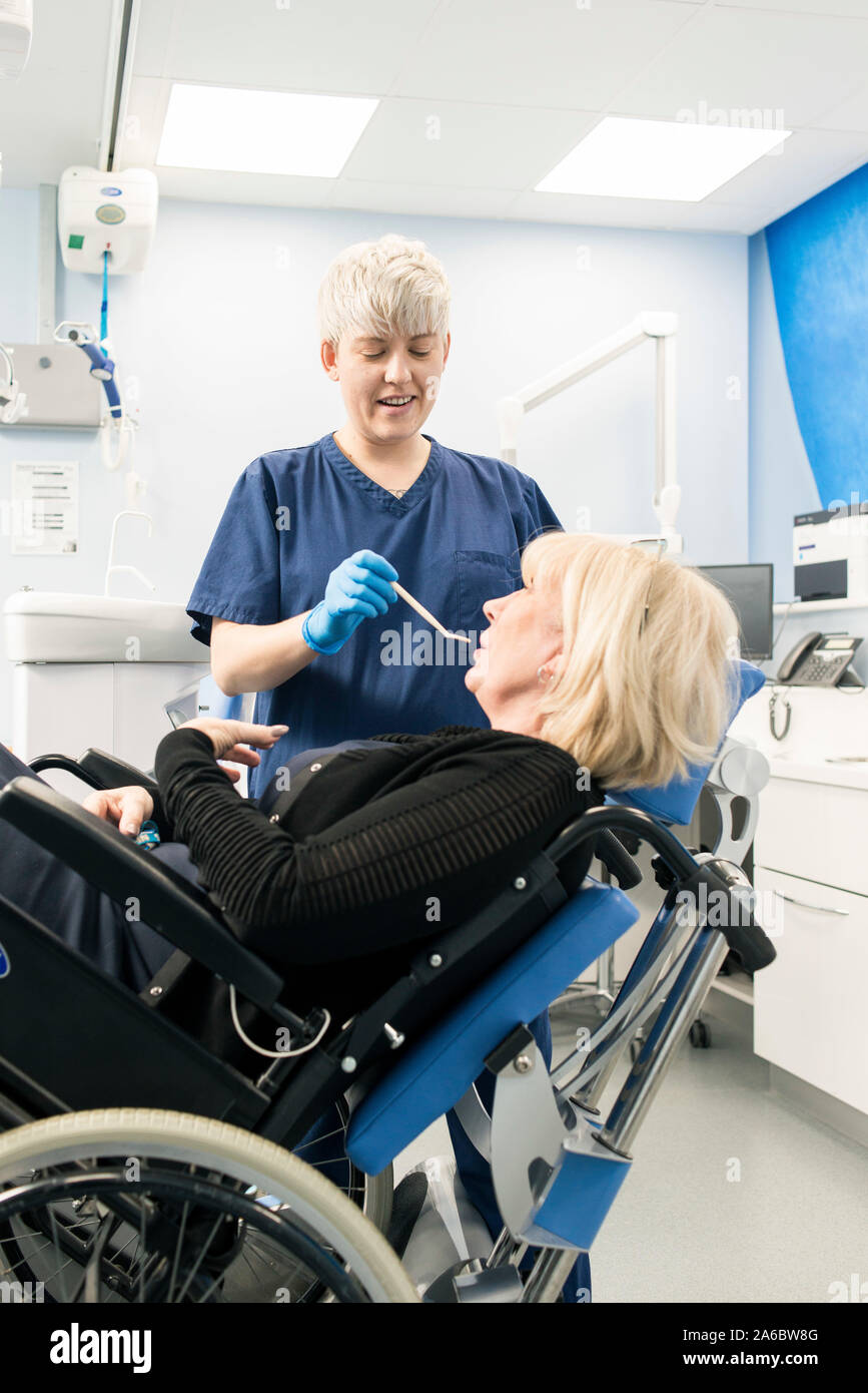 A dental nurse speaks to a disabled patient in a specialist wheelchair friendly dental chair Stock Photo