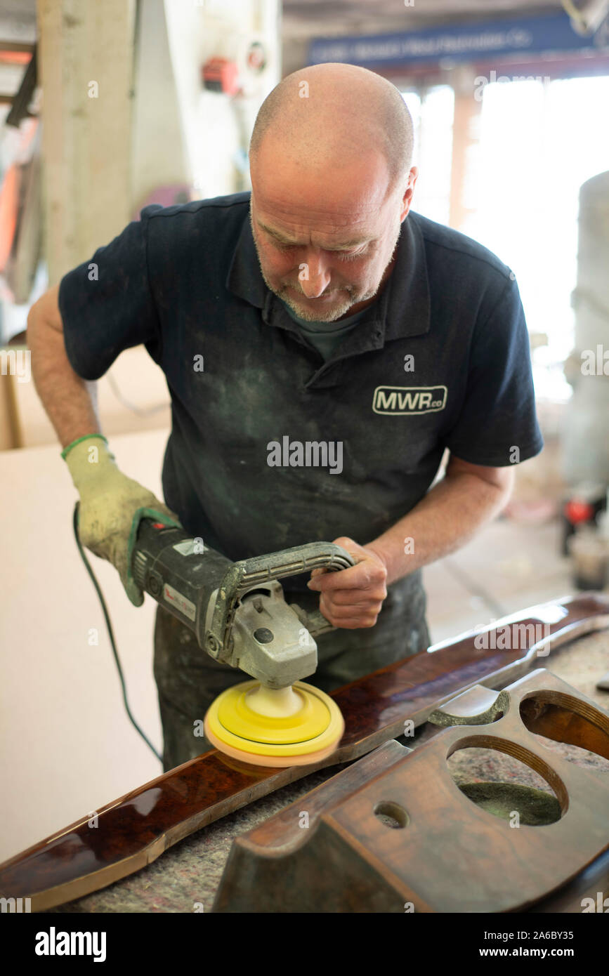 An expert woodwork car restorer polishes an old dashboard of a classic car Stock Photo