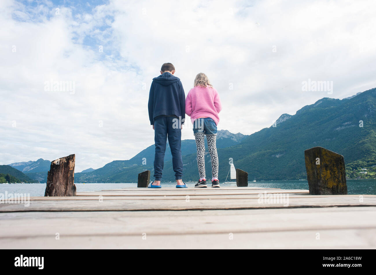 Two children who are brother and sister stand at the end of a jetty on lake annecy in france