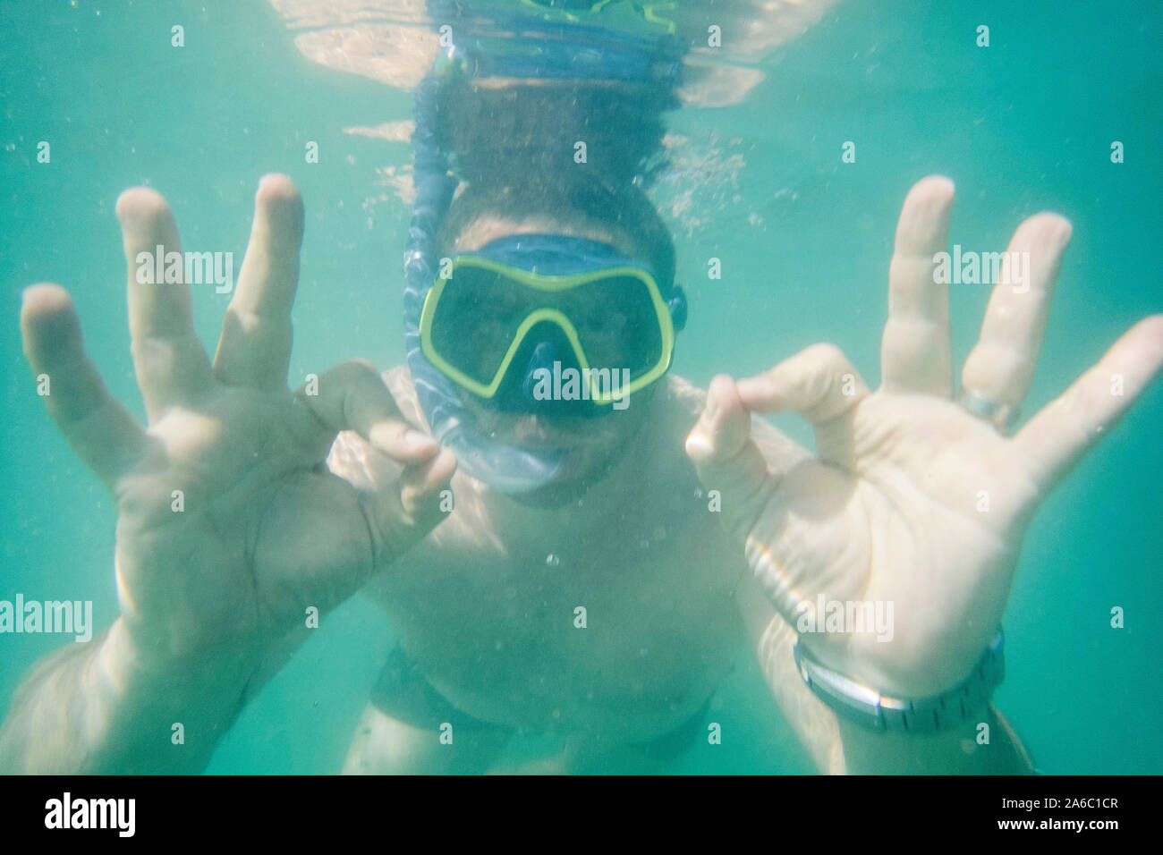 A man snorkelling underwater with a mask and snorkel signalling that he's ok Stock Photo