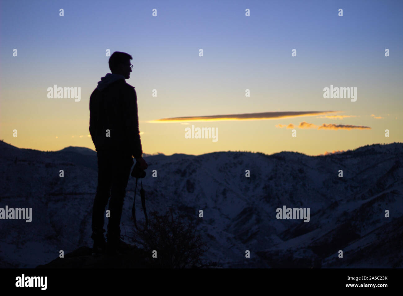 Silhouette of a man looking out over a cliff during sunset Stock Photo