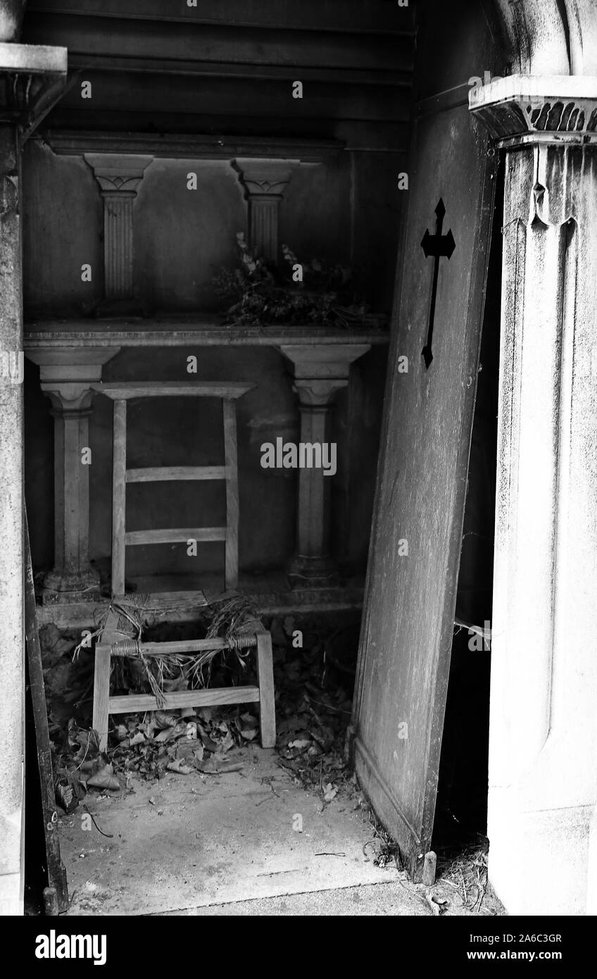 unhinged door and broken chair on burial plot of the cemetery Stock Photo