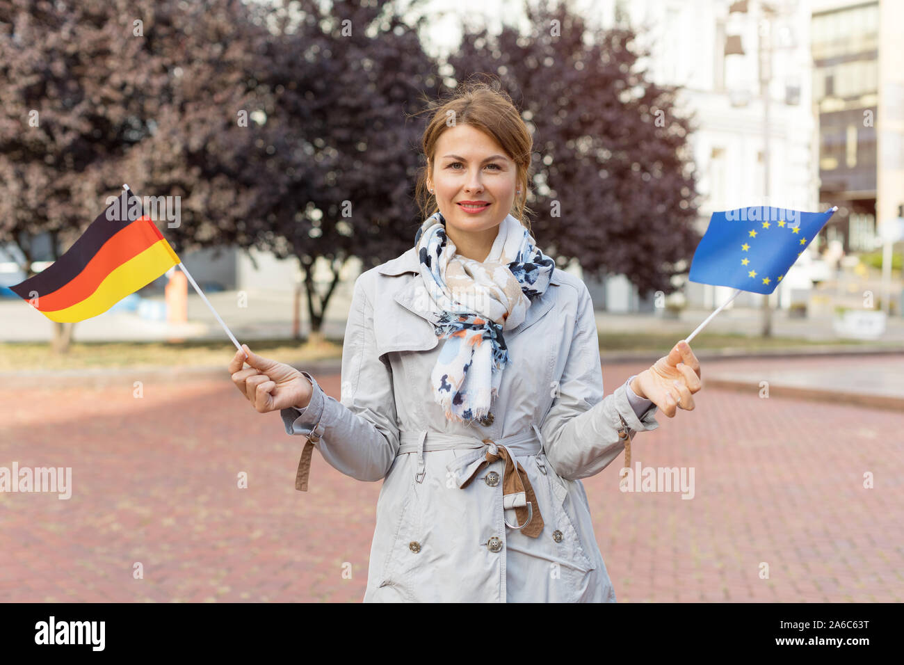 Middle-aged woman with flags of Germany and the European Union against the backdrop of the park and the city. Stock Photo