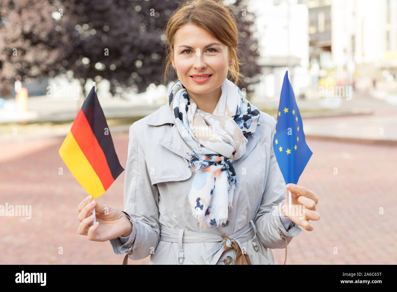 Middle-aged woman with flags of Germany and the European Union against the backdrop of the park and the city. Stock Photo