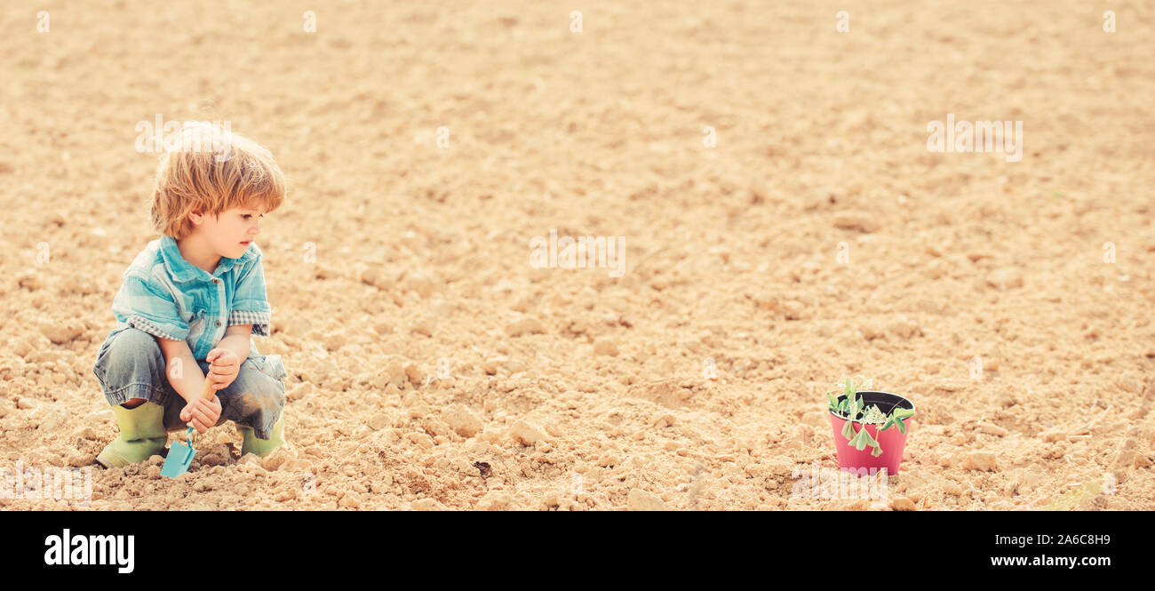 Child having fun with little shovel and plant in pot. Planting in field. Little helper in garden. Boy planting flower in field digging ground. Mother nature concept. Work at farm. Planting seedlings. Stock Photo