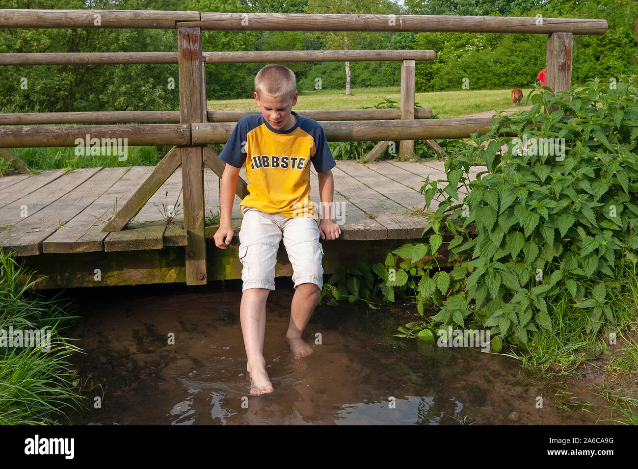 A young boy sitting on a bridge with his feet in the water. Stock Photo