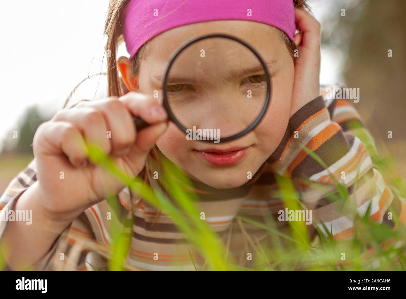 A young girl is looking at grass through a magnifying glass. Stock Photo