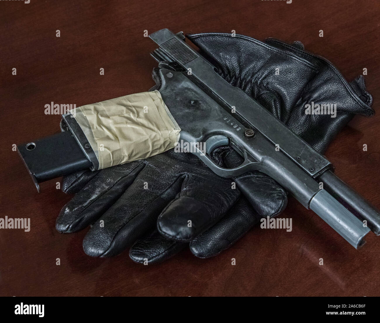 A illicit handgun placed on a pair of black leather gloves. Mafia.. Stock Photo