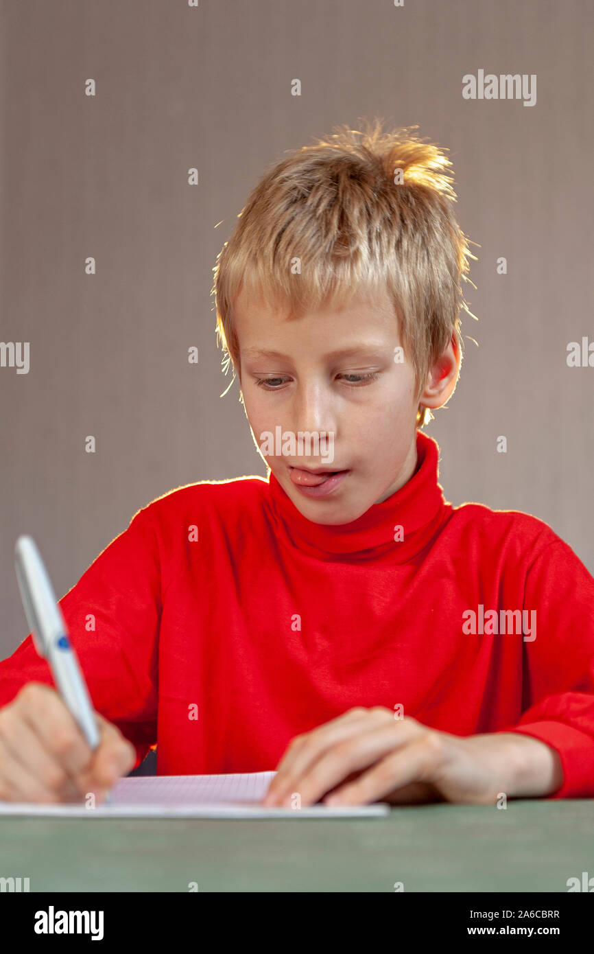 Portrait of a young fair boy concentrating on his writing with his tongue sticking out. Stock Photo