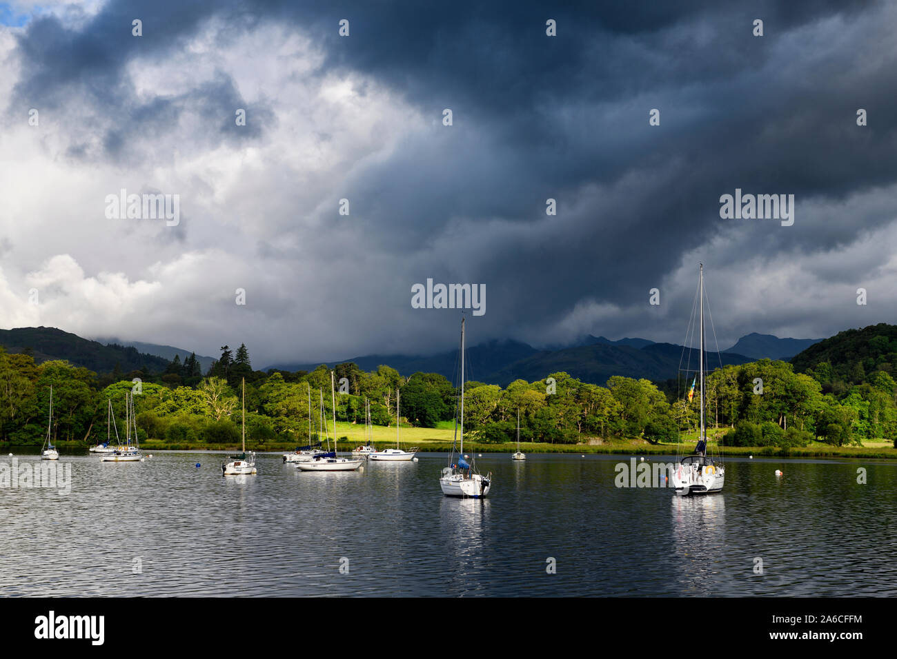 Sailboats moored on Lake Windermere at Waterhead Ambleside in morning sun with dark clouds Lake District National Park England Stock Photo