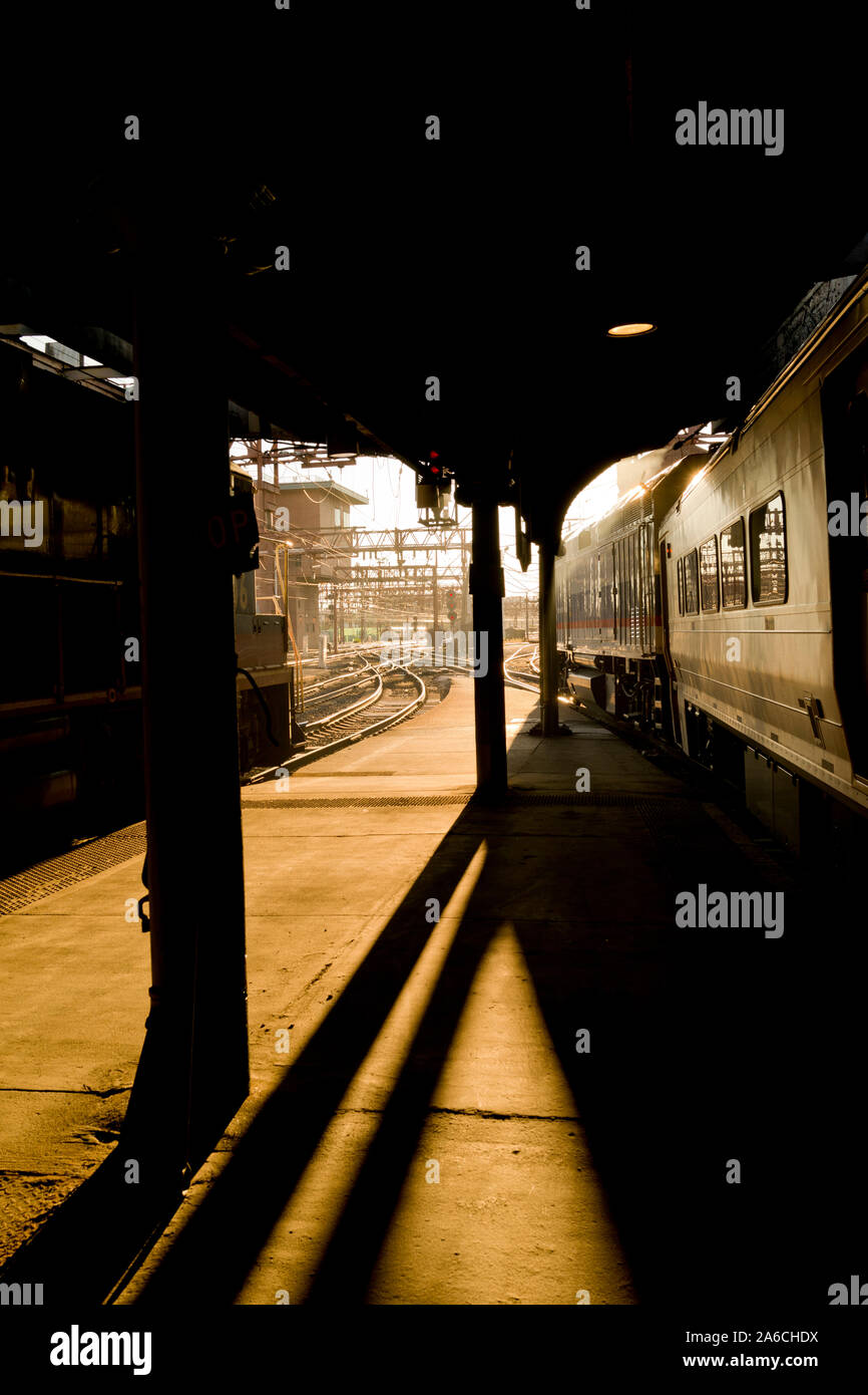 Dramatic afternoon light at the Hoboken Train Terminal.  Back light create strong shadows across the platform, train and tracks. Vertical color photog Stock Photo