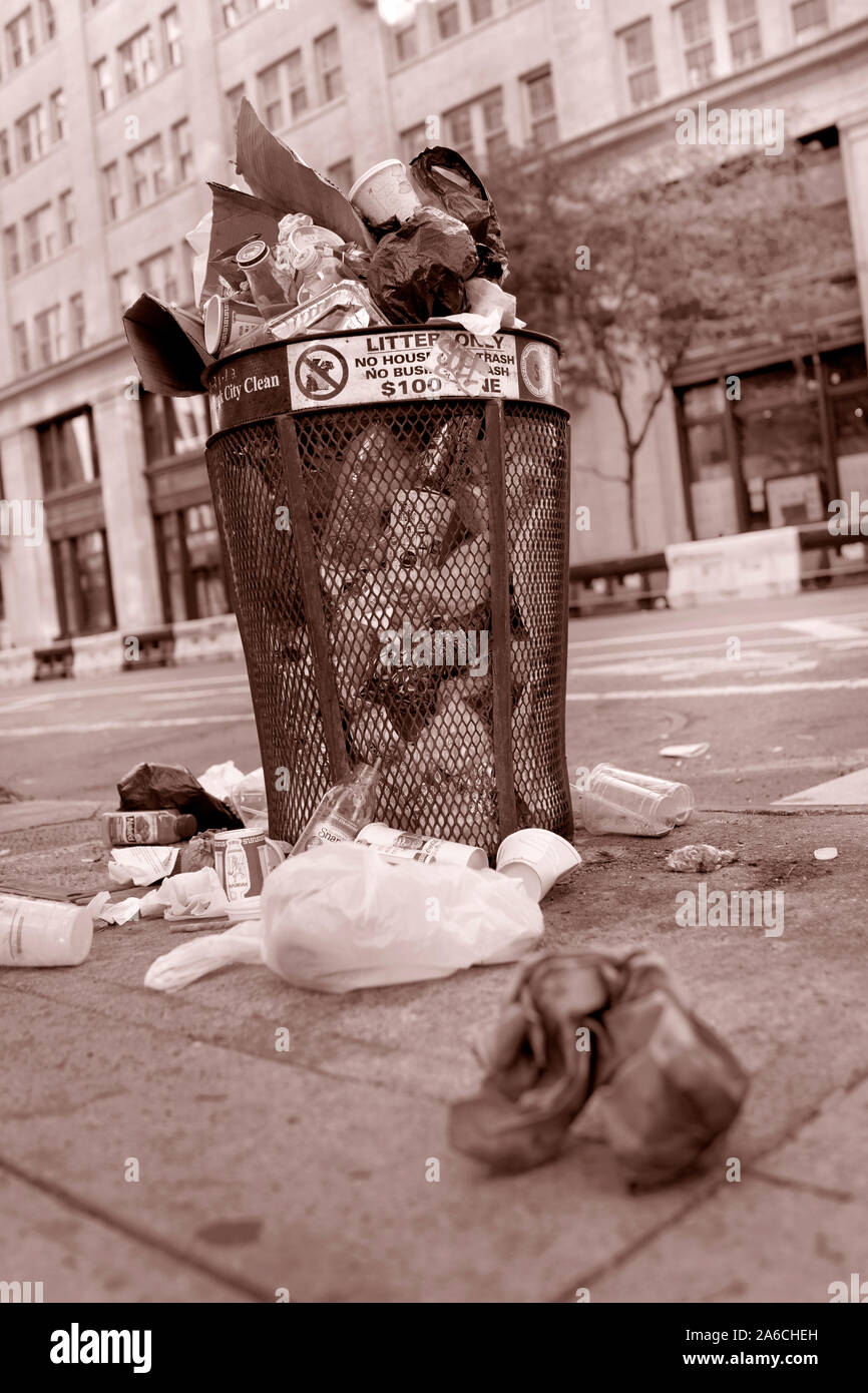 rash can overflowing on urban sidewalk.  Public waste bin full with plastic and paper bags and containers in street.  No people Stock Photo