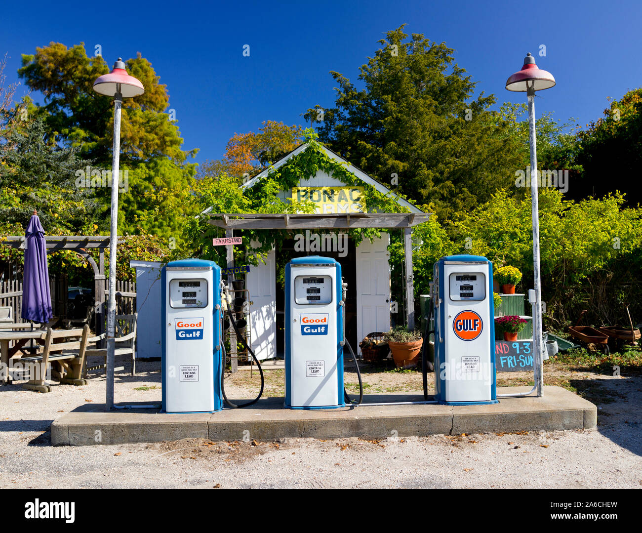 Three antique gas pumps with dirt road.  Small shed in rear.  Rural setting with trees and vines.  Full color horizontal photograph. Stock Photo