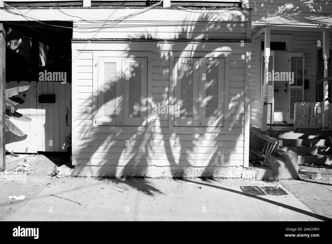 Strong shadow pattern of palm tree on one story island home with shuttered windows, clap board siding.  Conch house in Key West, FL USA Stock Photo