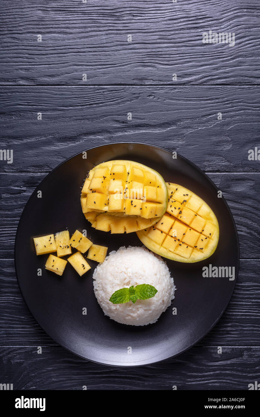 Sticky Rice With Mango on a black plate on a wooden table, thai cuisine, horizontal view from above, free space, flatlay Stock Photo