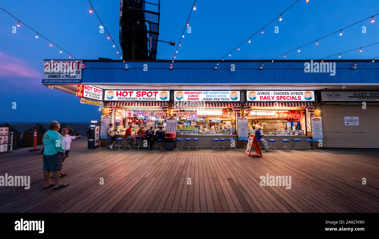 Few people walk and visit stores and game rooms on an empty boardwalk at night when summer is over. Stock Photo