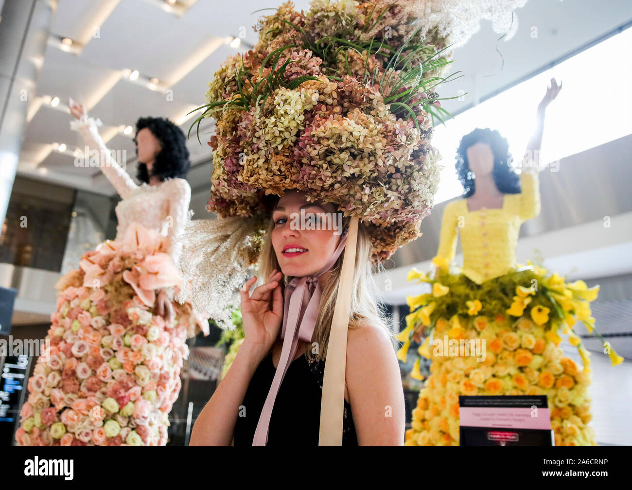 New York, USA. 25th Oct, 2019. A model with floral headpiece poses for a photo with mannequins with fresh-floral fashion at the Shops and Restaurants at Hudson Yards in New York, the United States, Oct. 25, 2019. A collection of 14 floral dressed mannequins curated by top NYC florists are on show during a free ten-day exhibition here from Oct. 25. The exhibition at Hudson Yards will be a part of Fleurs de Villes' 'Mannequin Series' partnering local florists with leading brands to create elaborate and original works of art. Credit: Wang Ying/Xinhua/Alamy Live News Stock Photo