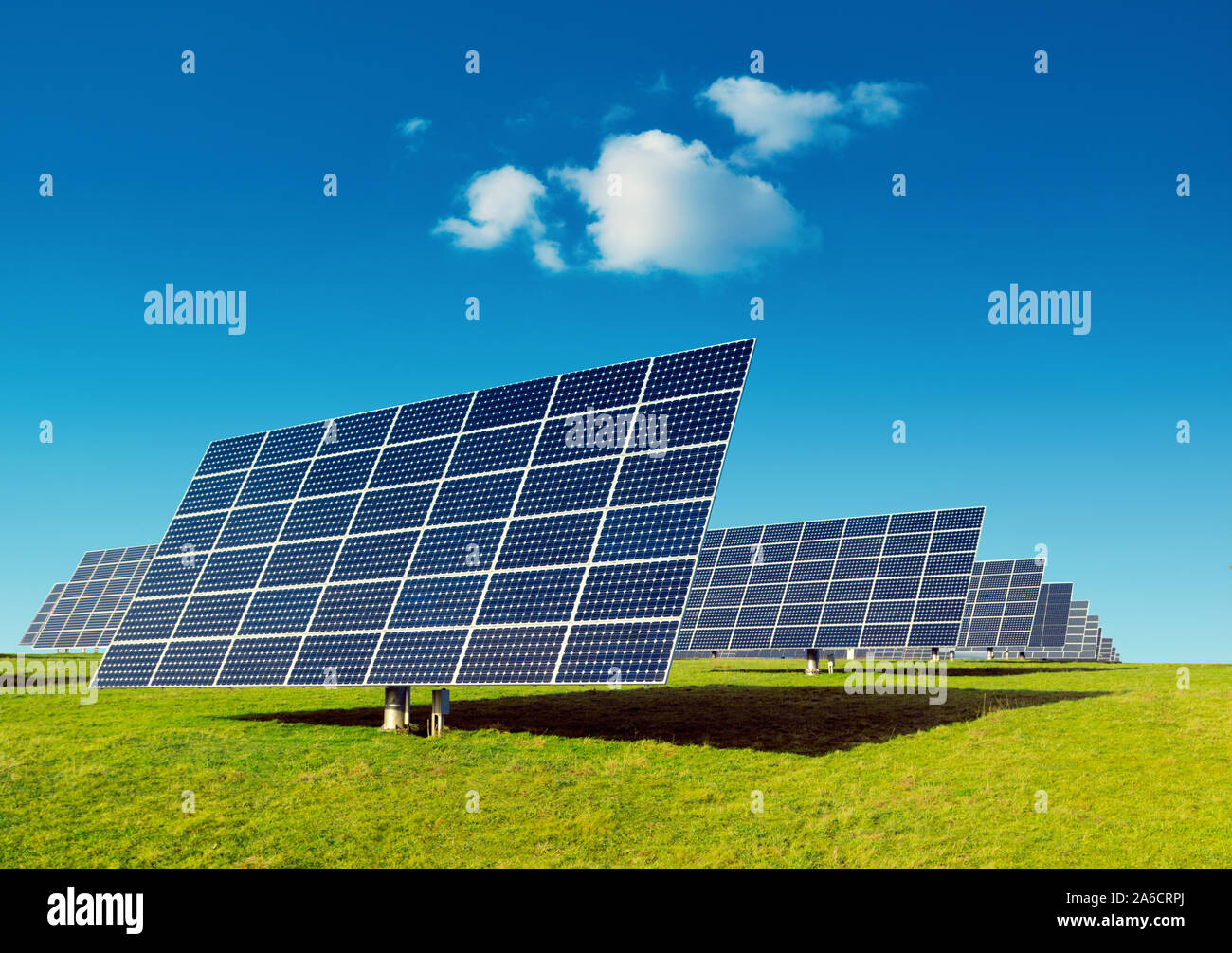 Rows of solar panels on a green grass field under blue sky with a small ...
