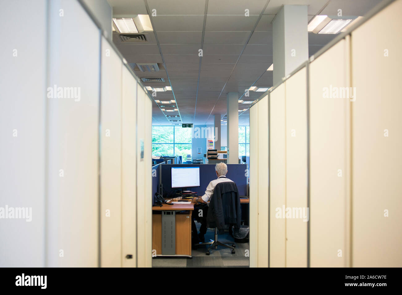 a member of staff sits at a desk working in a boring office Stock Photo