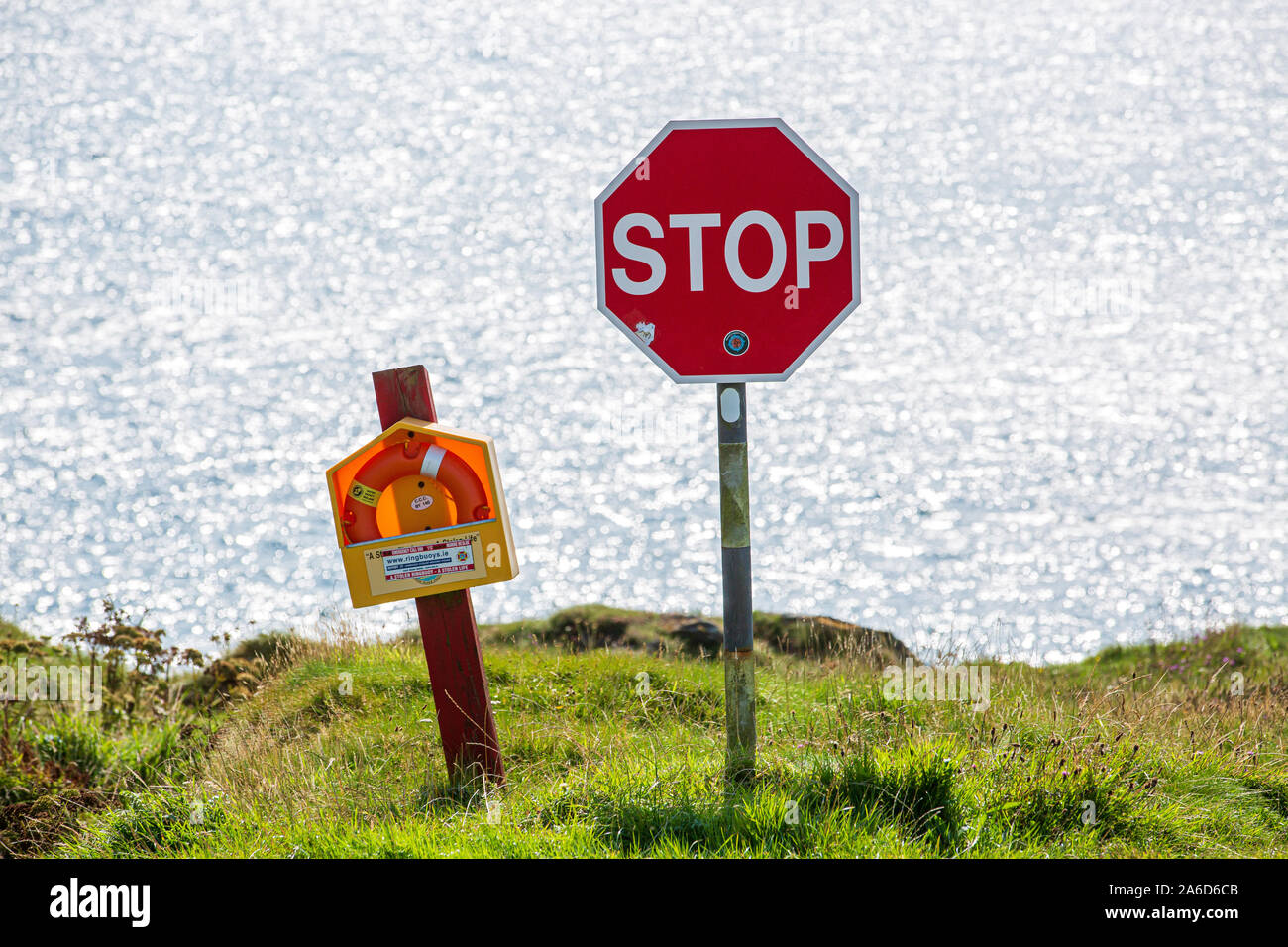 Stop sign and a rescue buoy at the end of the road on the verge of a cliff overlooking the ocean. County Cork, Ireland Stock Photo