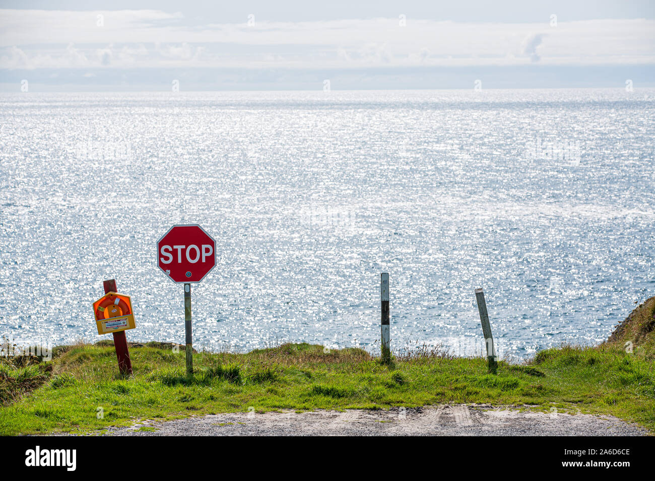 Abrupt end of the road at the verge of a cliff marked with a stop sign and a rescue buoy. County Cork, Ireland Stock Photo