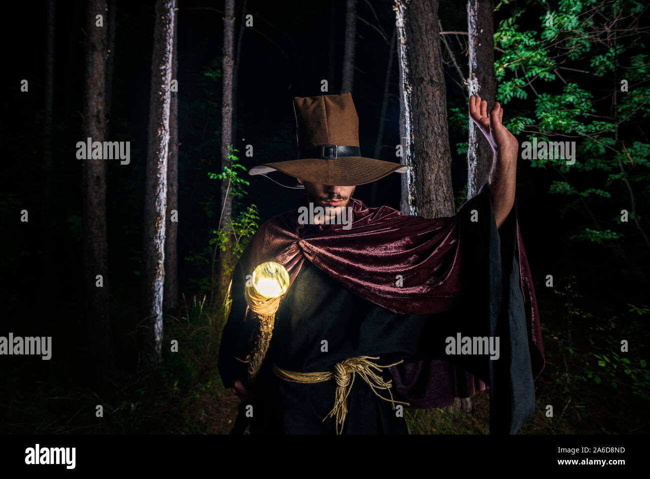 Man who is wearing wizard robes and casting glow spell with his magic staff in the woods Stock Photo